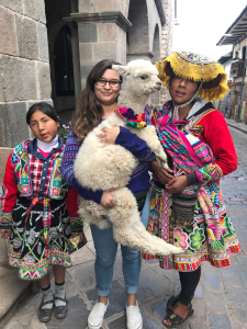 Georgiana holds a baby alpaca in Cusco, Peru, with a Peruvian mother and her daughter.